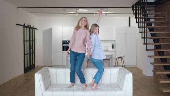 Happy Family Senior Mom Having Fun with Adult Daughter Dancing on Sofa in Living Room alt