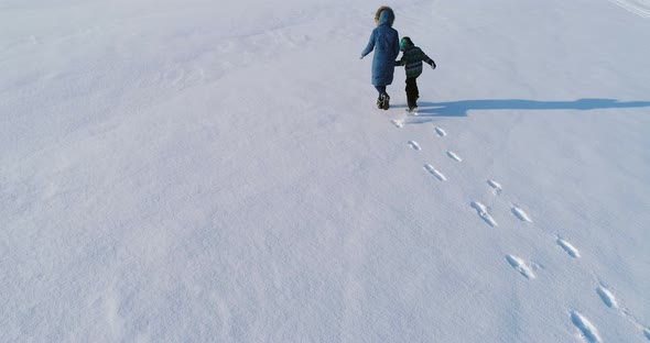 Family Time Walk and Play Together. Mother and Son Running Hand in Hand Through the Snow Covered