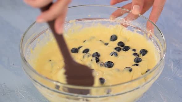 Woman hold spatula and mixing batter with blueberry.