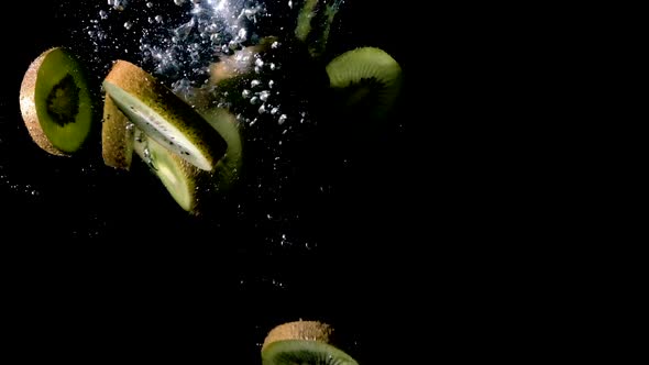 Kiwis dropped into water on black background, side lit slow motion alt