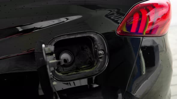 a woman's hand inserts a pistol into the tank to fill the car with gasoline or diesel fuel. alt