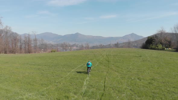Aerial: man having fun by riding mountain bike in the grass on sunny day, scenic alpine landscape, alt