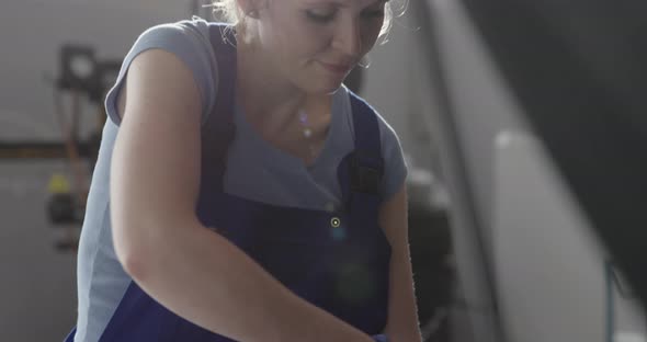 Confident female mechanic fixing a car in the auto repair shop, car servicing concept