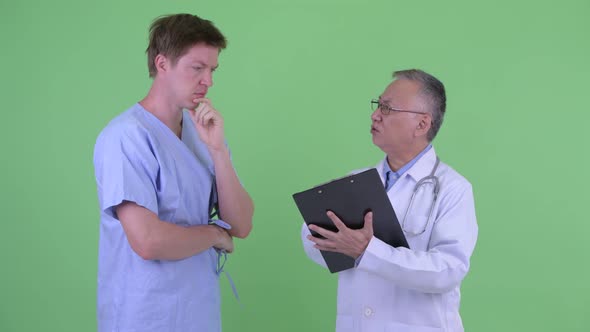 Stressed Mature Japanese Man Doctor with Young Man Patient Getting Bad News Together alt