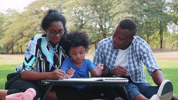 Happy African American Parents teach son to made homework in the park
