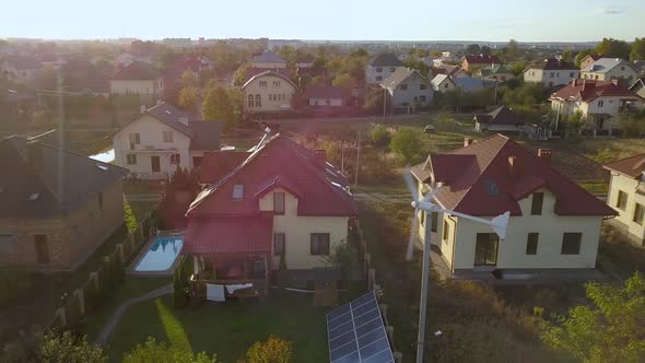 Aerial view of a residential private house with solar panels on roof and wind generator turbine alt