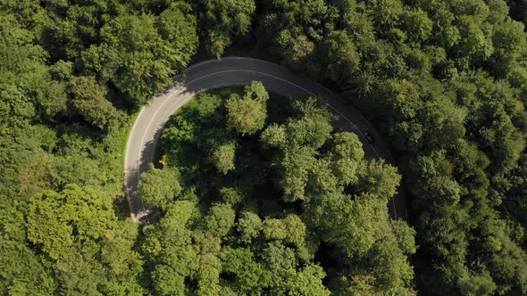 A transporter car is driving into a tight serpentine curve in a green  forest, drone shot zooming sl alt