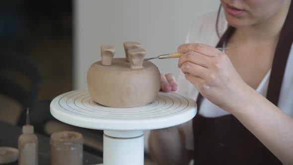 Close Up of Female Hands Holding Stick and Making Ornament on Earthenware. Clay Master Moulding Clay alt