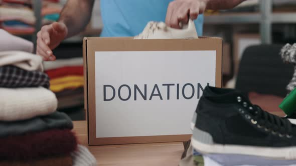 Male Volunteer Sorting Shoes and Putting It Into the Cupboard Box at the Warehouse alt