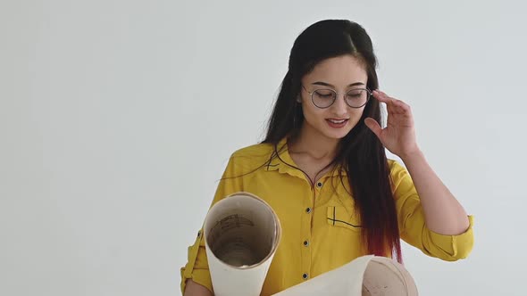 Asian woman architect in glasses with drawings in hands on  plans smiles camera alt