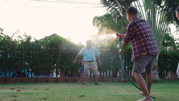 Happy Family playing together during Retired Grandfather watering the plants at the home garden. alt