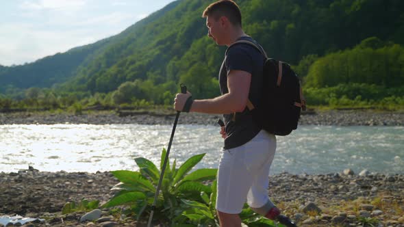 Male Backpacker with Prosthetic Leg is Strolling Over Shore of River in Summertime alt