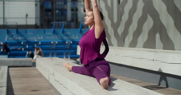 Athletic Woman Sits on a Twine on the Bench and Does Dends Forward, Stretching in the Yard of an alt