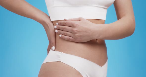 Close Up Shot of Woman Touching Her Back Feeling Kidney Inflammation Blue Studio Background alt