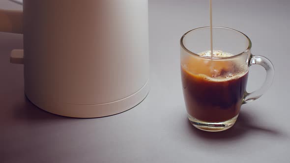 Cream is poured into coffee, next to the electric kettle is alt