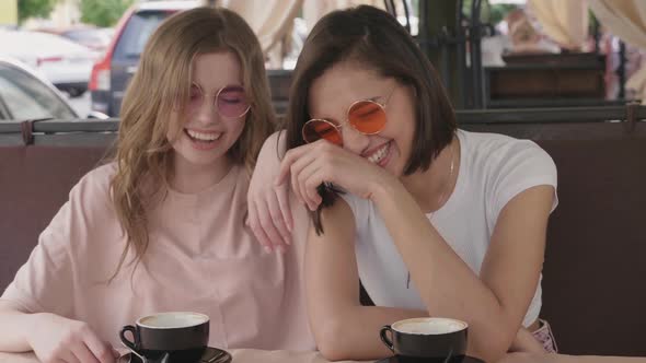 Two young beautiful smiling hipster girls chatting in cafe alt