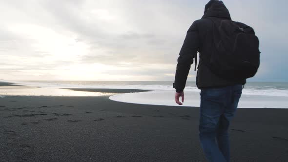 Man Traveler Walking on Volcanic Black Sand Beach in Iceland alt