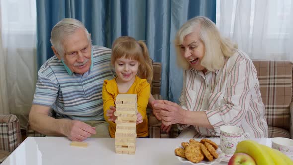 Excited Child Girl Kid Involved in Build Blocks Board Game with Senior Grandmother and Grandfather alt
