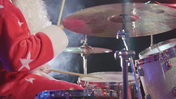 Side View of Drummer in Carnival Costume of Santa Claus with a Beard Beats with Sticks on Drums and alt