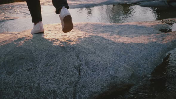 Back View of Female Legs Carefully Stepping Over Small Beautiful Water Stream on a Rock alt