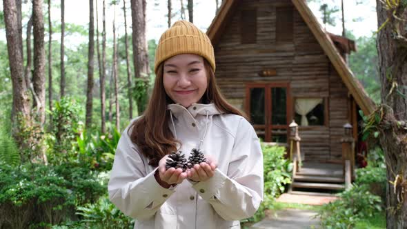 Closeup of a female traveler holding and showing pine cone in her hands in the forest