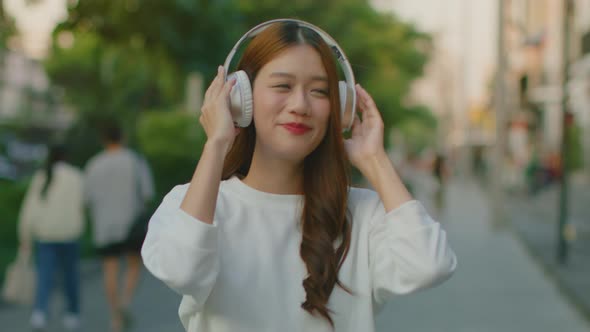 Happy Asian woman in headphones walking in the city street outdoor having fun listening to music