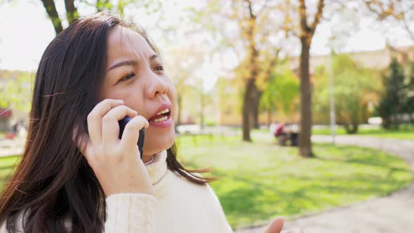 Close up of Asian black straight woman standing at the park and talking smartphone alt