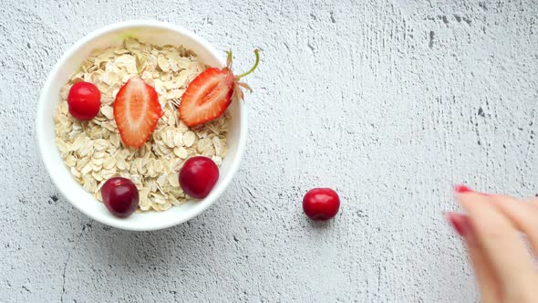 Detail Shot of a Kitchen Table with a White Cup of Oatmeal and Strawberries and a Hand That Lays alt