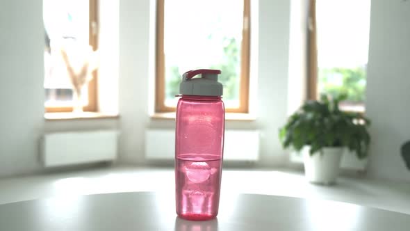 Woman Taking Pink Plastic Bottle of Water From Table in Bright Room Closeup