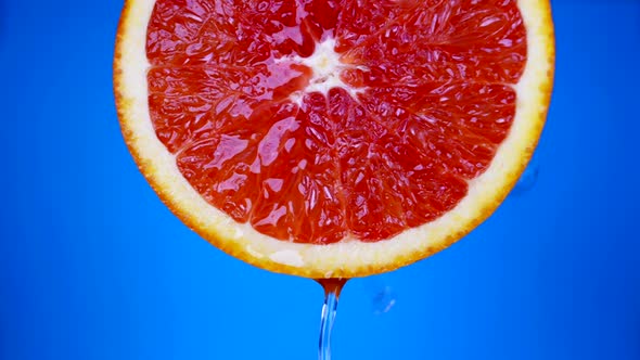Juicy Grapefruit in Blue Background Closeup Fresh Cool Water is Pouring Over Bright Red Pulp alt