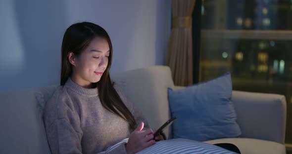 Woman look at mobile phone and sit on sofa at night