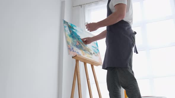 A Young Male Artist Works in a Studio He Uses Bright Paint on a Large White Canvas alt