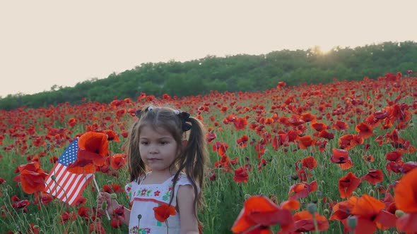 American baby girl with the US flag. Independence Day. Poppies field at sunset alt