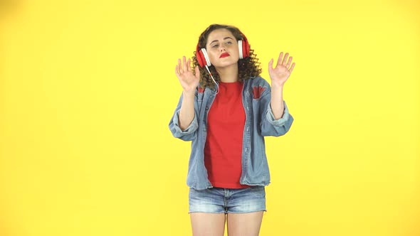 Lovely Girl Dancing in Big Red Headphones on Yellow Background at Studio alt