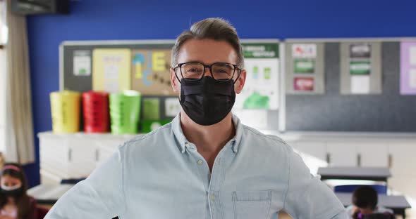 Portrait of caucasian male teacher wearing face mask in the class at school alt