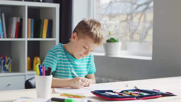 Boy is Doing  Homework at the Table. Cute Child is Learning at Home. alt