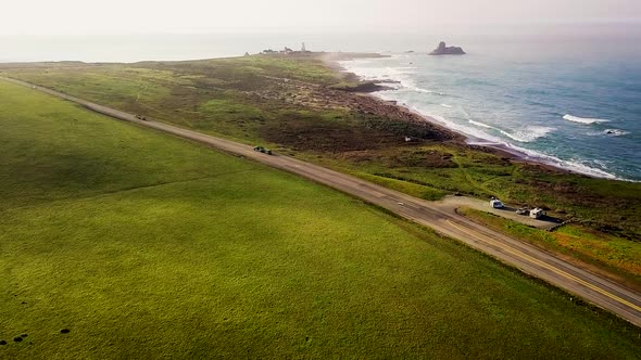 Vehicles drive the Cabrillo Highway at Piedras Blancas Lighthouse on the California coast alt