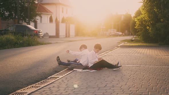 Schoolboys Sit on Street Sidewalk Surrounded By Books alt