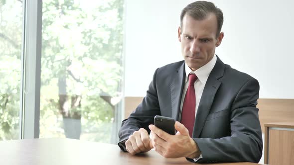 Shocked Astonished Businessman Using Smartphone alt