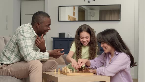 Happy Family of Three People of Different Races Play Chess at Home in the Living Room alt