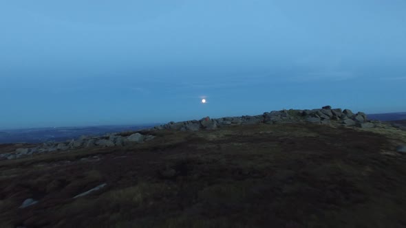 Aerial shot of men climbing boulders while bouldering at night under a full moon. alt
