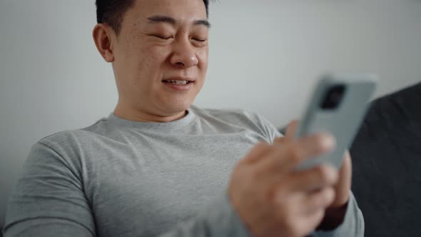 Laughing Asian man texting by phone alt