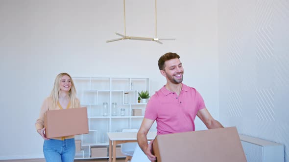 Excited blonde young woman and bearded guy stack cardboard boxes on large pile alt
