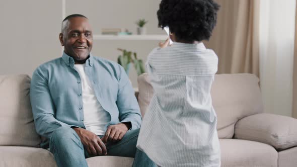 African American Man Sitting on Sofa in Room Accepting Congratulations Caring Daughter Gives Card to alt