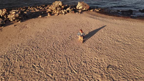 Flight Up: Serious LGBT Woman Wears Rainbow Bracelet and Sits at Cape Kolka with View Over Sea alt