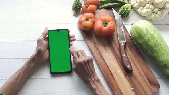 Senior Women Hand Using Smart Phone and Fresh Vegetables on Table alt