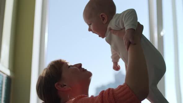 Happy Young Mother Throws Her Baby Up and Kisses alt