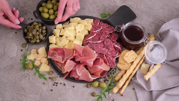 Making Meat and Cheese Antipasto Plater Woman Adding Capers and Olives to Serving Board with Cheese alt