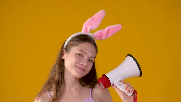 Portrait of a happy young girl in pink bunny ears talking with megaphone