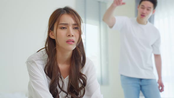 Asian young couple sitting on bed with painful after fight argument. alt